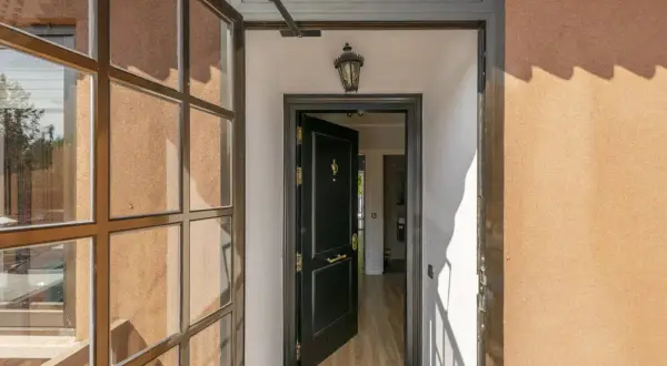 Puerta principal negra abierta, con ventana lateral y luz de porche. Ideas para cerrar un porche con estilo moderno.
