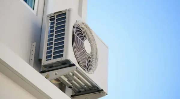 Unidad exterior de aire acondicionado montada en pared blanca, ideal para saber donde colocar la unidad exterior del aire acondicionado para una ventilación óptima.