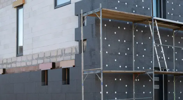 Fachada de edificio en construcción con aislamiento de poliestireno expandido gris, conocido como llana mineral, y andamios.
