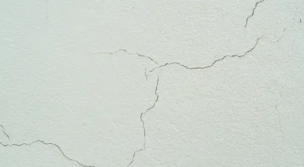 Detalle de grietas finas en una fachada de color crema, mostrando el paso del tiempo y la textura del material.