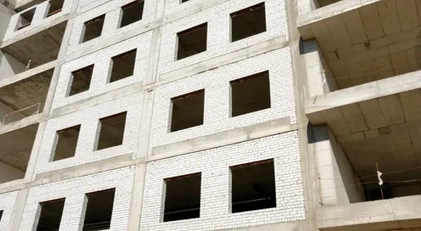 Fachada monocapa blanco de edificio en construcción, con ventanas vacías y balcones de hormigón.