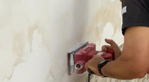 Hombre lijando pared con manchas de humedad para arreglar humedades.