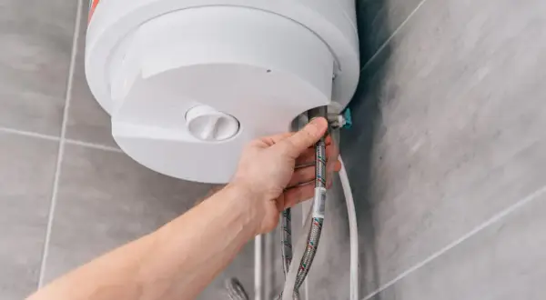 Mano conectando mangueras a un termo eléctrico. Guía para saber como vaciar un termo eléctrico de forma segura.