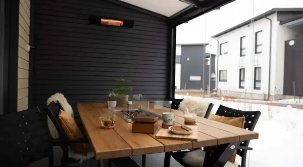 Mesa de madera en terraza cerrada con calefactor, ideal para disfrutar de una bebida caliente en invierno.