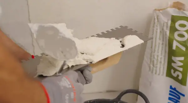 Man applying morteros para fachadas con llana dentada. Bolsa de producto de construcción al fondo.