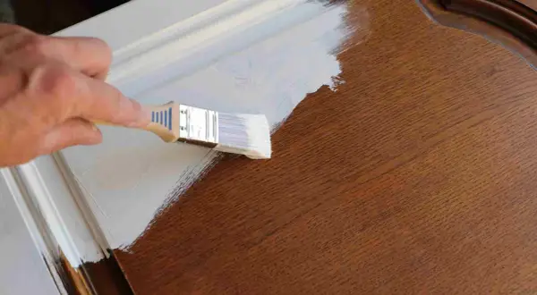 Mano pintando una puerta de madera con brocha blanca. El proceso de pintar puertas de madera es un proyecto de bricolaje común.
