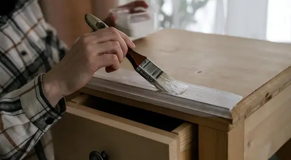 Persona aplicando pintura blanca a un armario de madera con un pincel. Paso a paso como pintar un armario de madera.