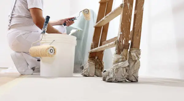 Pintor prepara cubos con rodillos para pintar. Se aprecian distintos tipos de rodillos para pintar, una escalera y cubos de pintura.