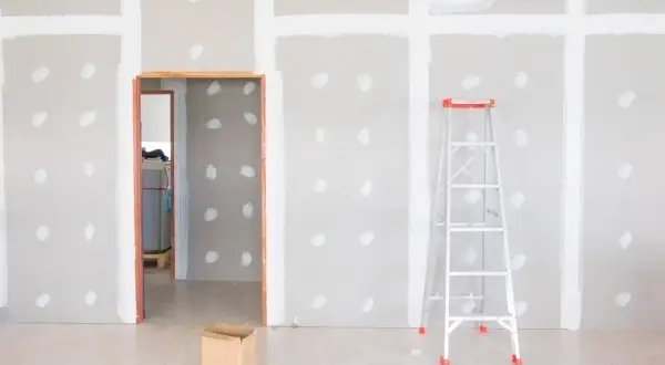 Habitación en construcción con paredes de enfoscado de yeso, una escalera y una caja de cartón.