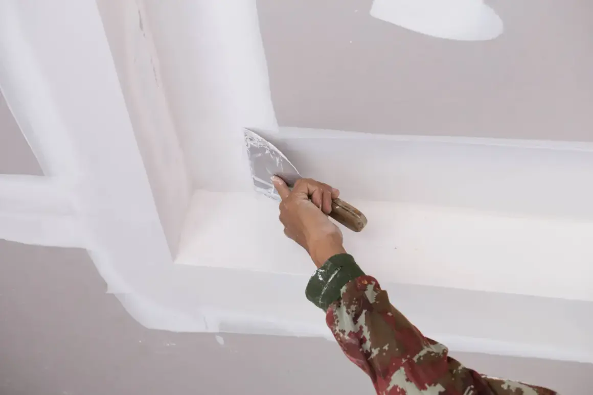 Mano con espátula aplica masilla para reparar techo escayola.