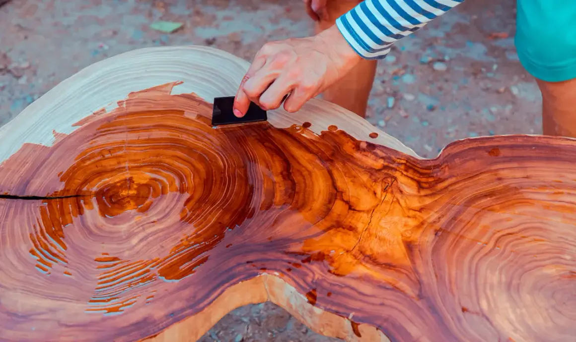 Mano aplica aceite de linaza a una mesa de madera rústica, resaltando sus vetas naturales.