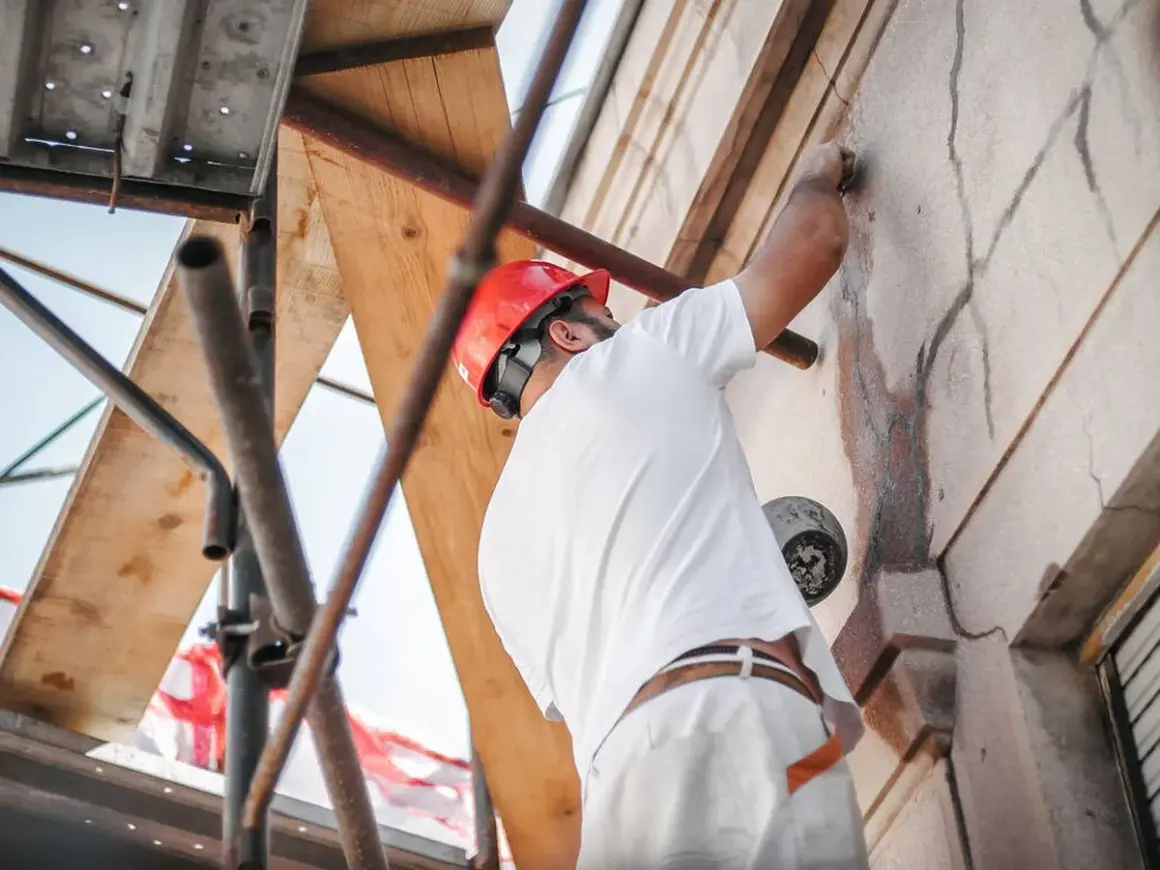 Trabajador con casco rojo repara grietas en fachada, cumpliendo la ley de propiedad horizontal.