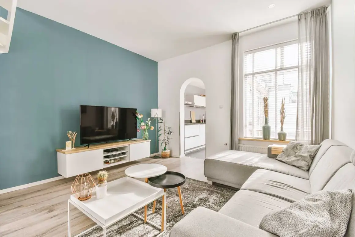 Ideas pintar salón en dos colores: pared azul verdoso y blanca, con sofá gris y muebles modernos.