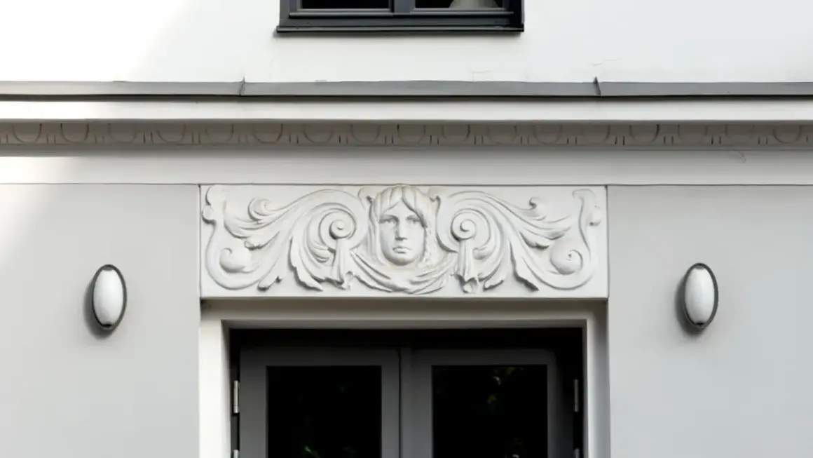 Detalle arquitectónico: una cornisa con un rostro femenino y volutas decorativas sobre una puerta.
