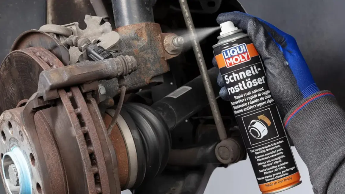 Mano enguantada rocía un spray para saber como quitar el óxido del metal en un componente de coche oxidado.