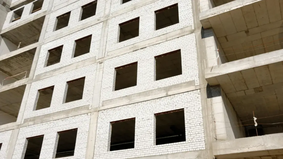 Fachada monocapa blanco de edificio en construcción, con ventanas vacías y balcones de hormigón.