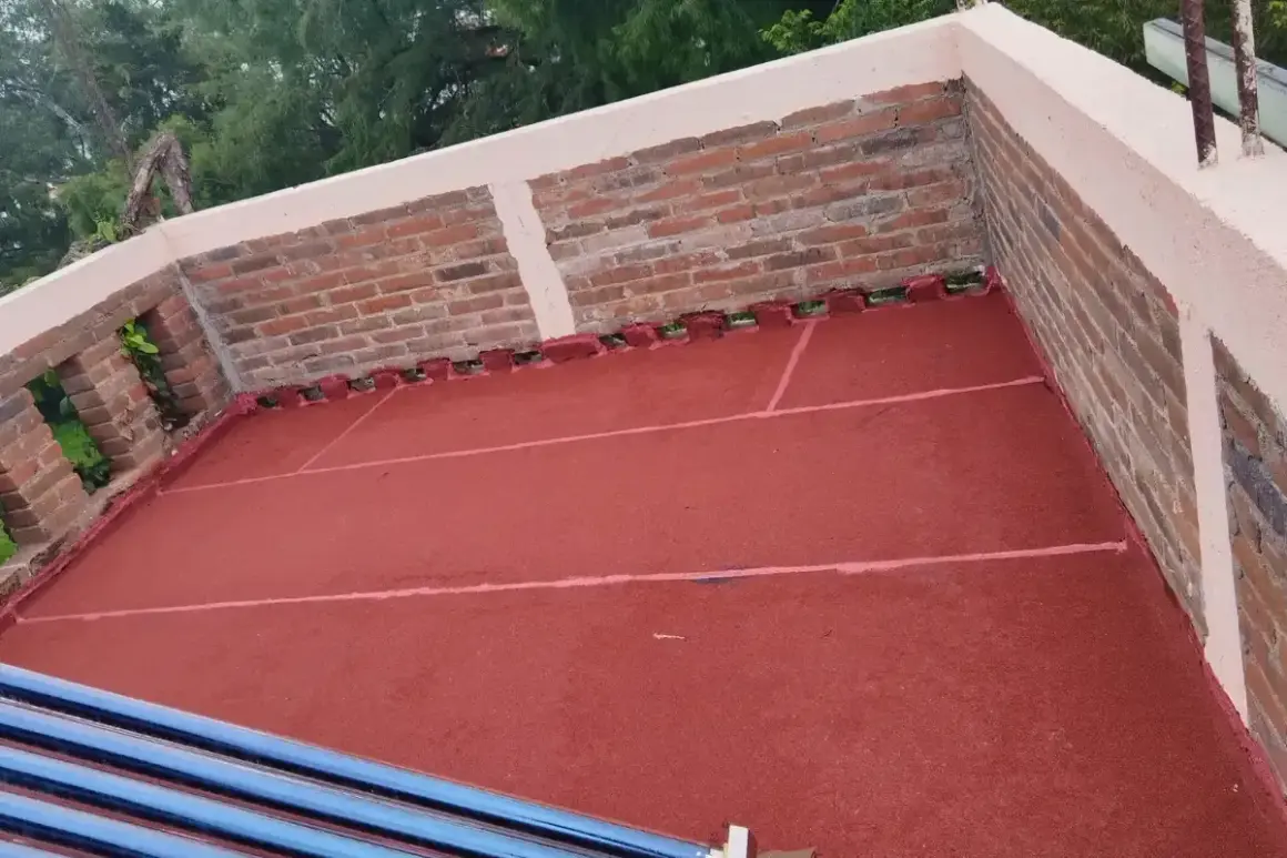 Terraza con pintura impermeabilizante roja recién aplicada. Se aprecian ladrillos y tubos de calentador solar.