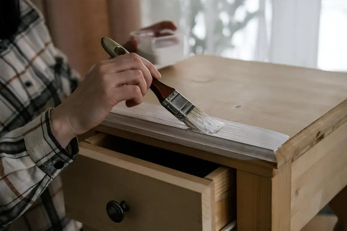 Persona aplicando pintura blanca a un armario de madera con un pincel. Paso a paso como pintar un armario de madera.