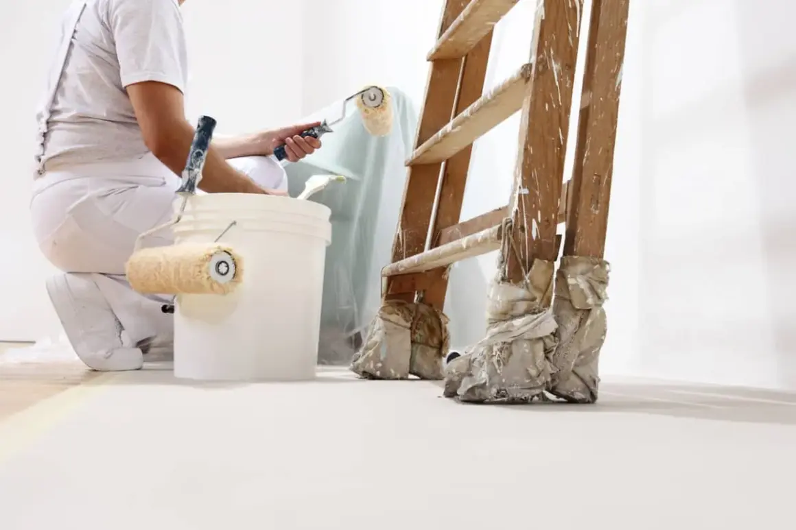 Pintor prepara cubos con rodillos para pintar. Se aprecian distintos tipos de rodillos para pintar, una escalera y cubos de pintura.