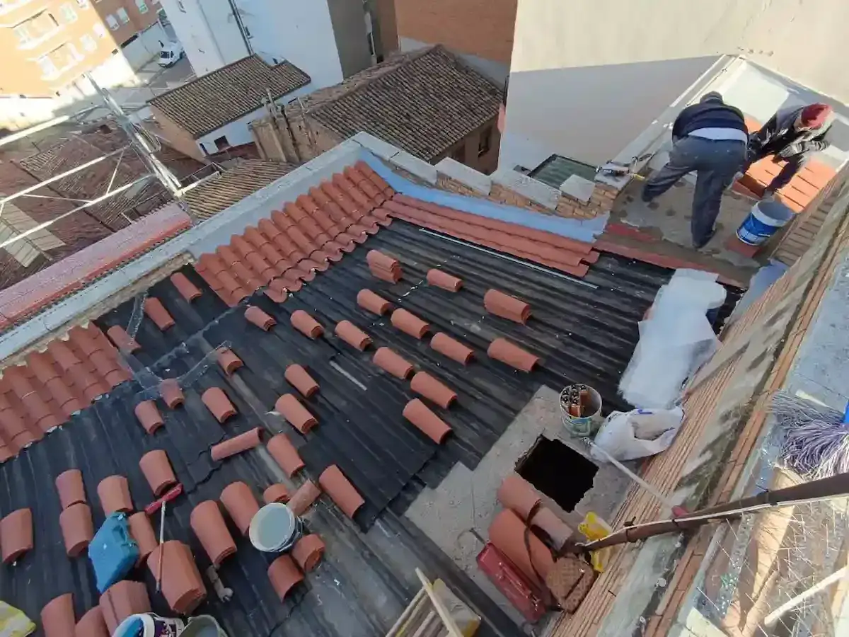 Trabajadores en un tejado antiguo, colocando tejas y preparando para impermeabilizar.