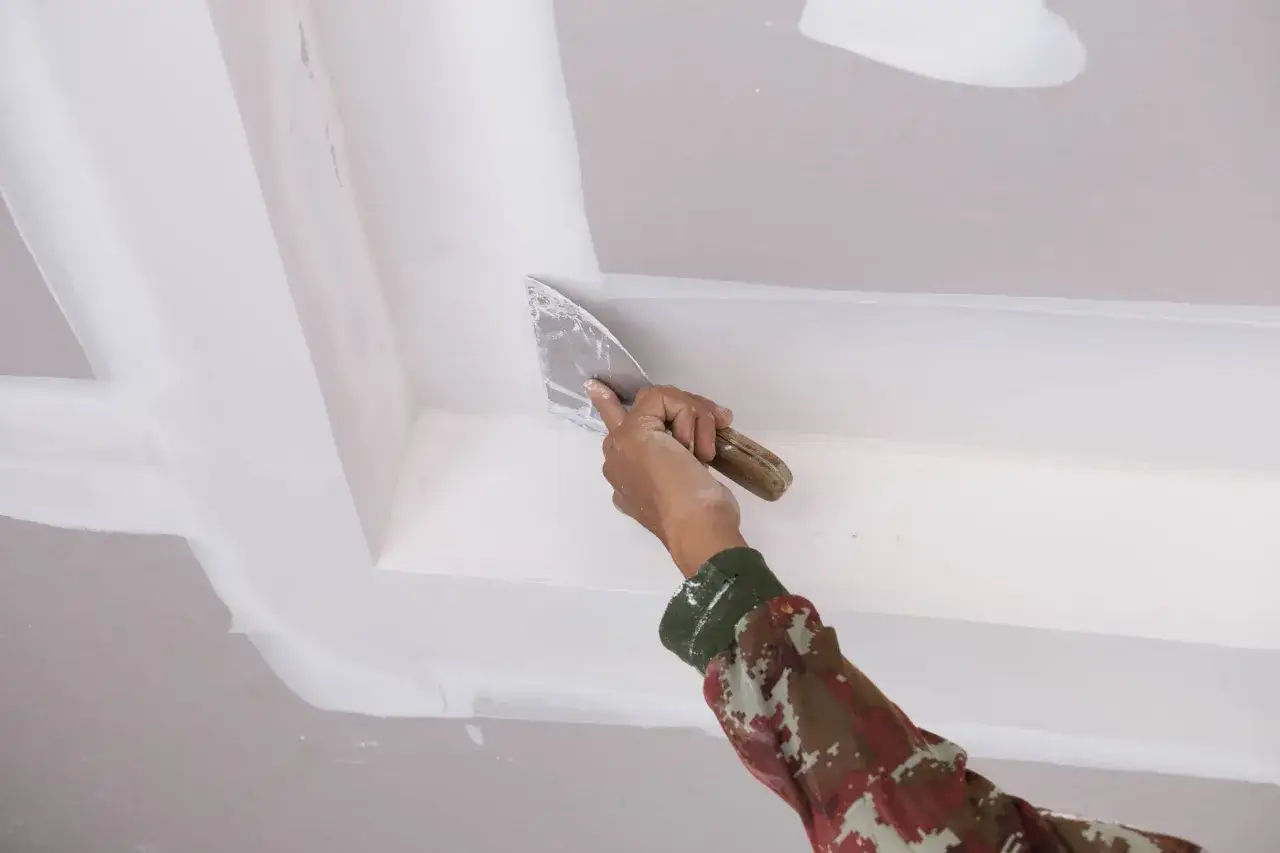 Mano con espátula aplica masilla para reparar techo escayola.