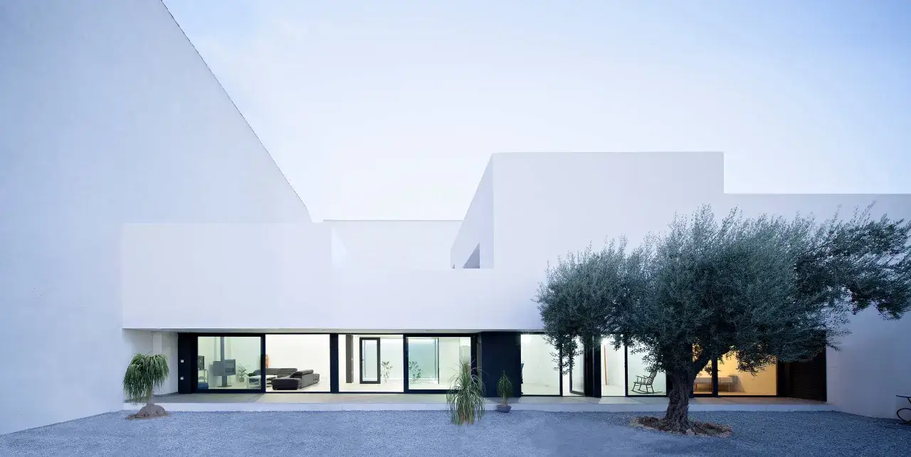 Fachada monocapa blanco de arquitectura moderna con grandes ventanales y un olivo centenario.