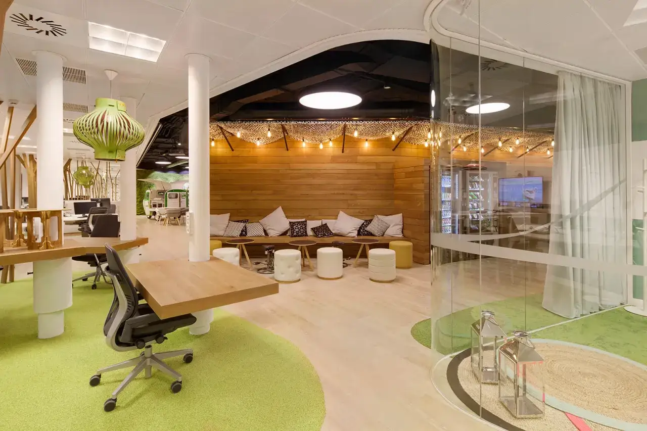 Espacio de oficina moderno con alfombra verde, asientos de madera y lámparas colgantes. Un ejemplo de diseño que busca la certificación WELL.