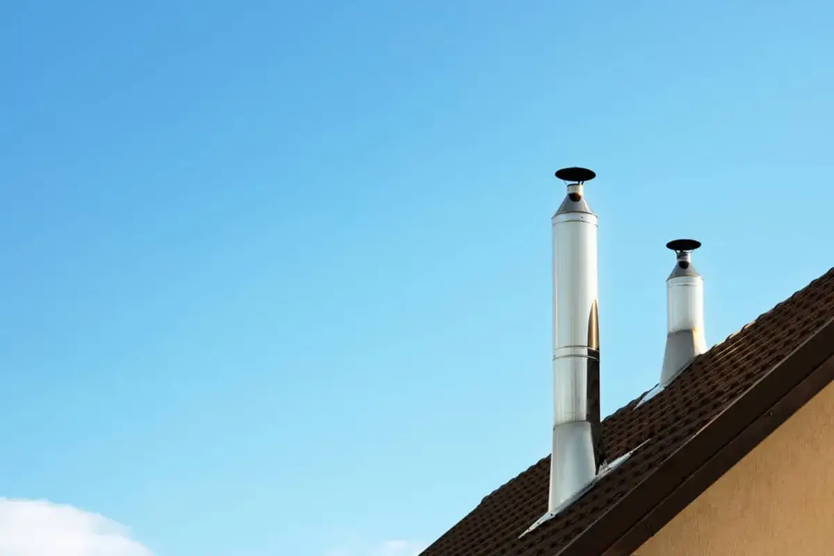 Dos tubos de chimenea metálicos sobre un tejado, listos para evacuar el humo y mantener una temperatura agradable en el hogar con leña.