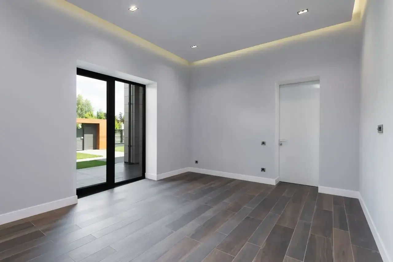 Habitación moderna con suelo de madera oscura, puerta blanca y focos empotrados sin falso techo.