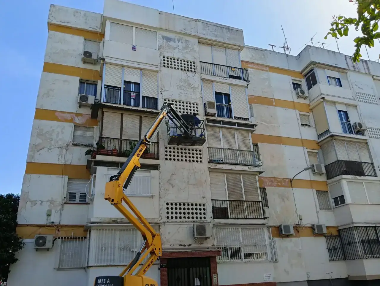 Trabajadores en plataforma elevadora realizan el arreglo de fachada de un edificio, cumpliendo la ley de propiedad horizontal.