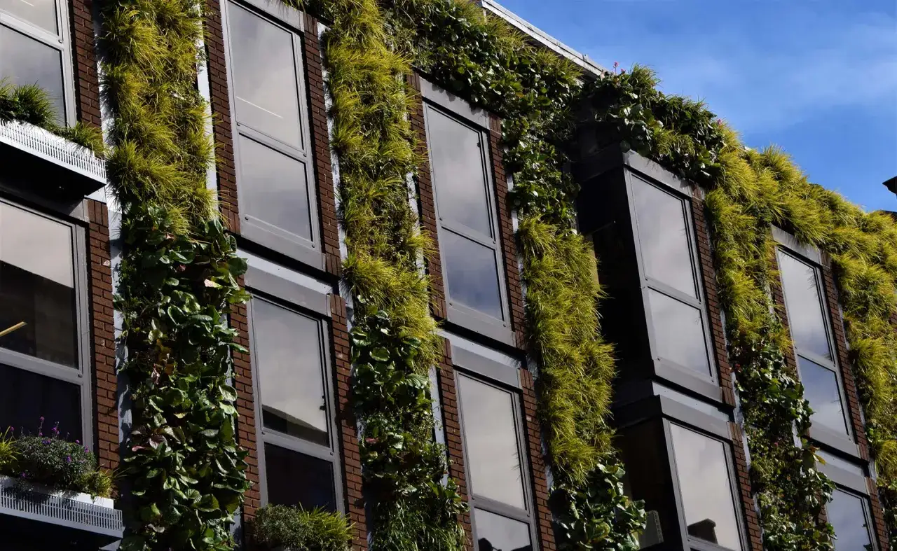 Edificio con fachadas verdes, un ejemplo de sostenibilidad en la construcción. Plantas trepadoras y césped cubren ladrillos y ventanas.
