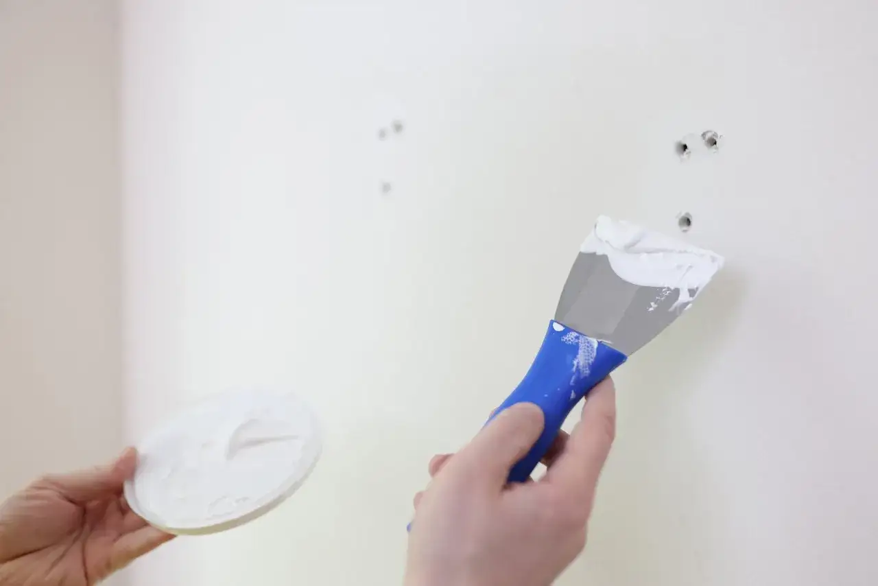 Mano aplicando masilla con espátula para alisar paredes y reparar agujeros.