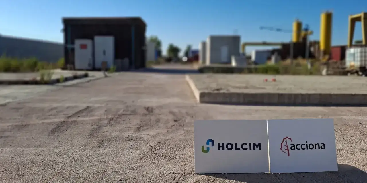 Dos carteles con los logos de Holcim y Acciona, empresas del MBCC Group, en un área industrial.