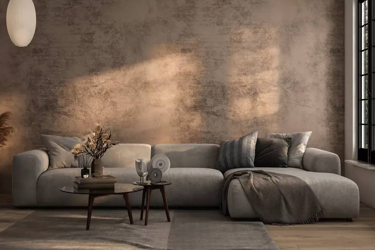 Sofá gris con cojines y manta, mesa de centro con libros y decoración. Pared con textura que recuerda a hacer gotelé con esponja.
