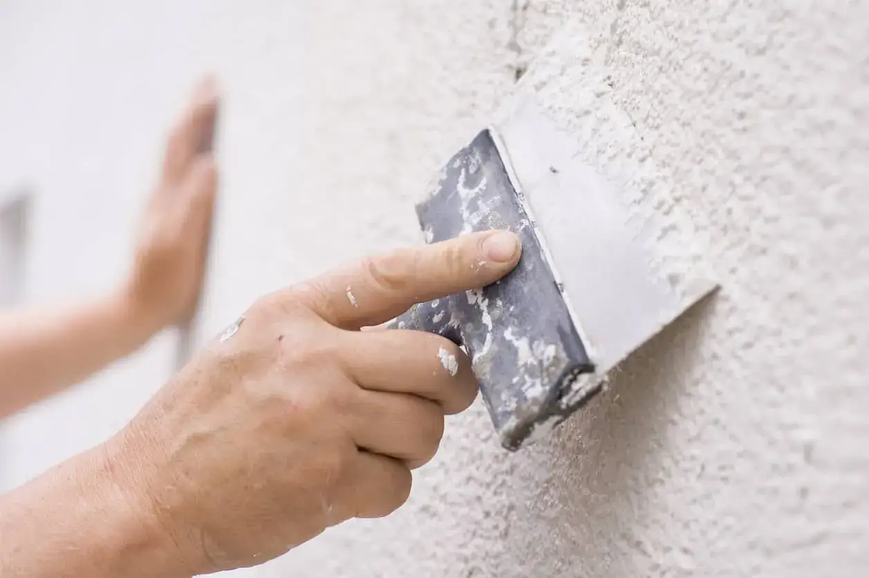 Mano aplicando masa para reparar gotele en pared texturizada.