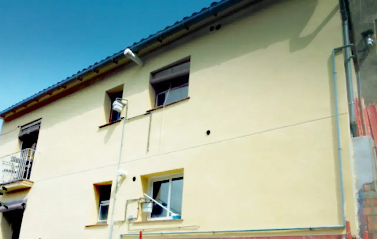 Fachada de edificio con acabado liso y color crema, con ventanas y balcón. Se busca el mejor mortero para fachadas exteriores.
