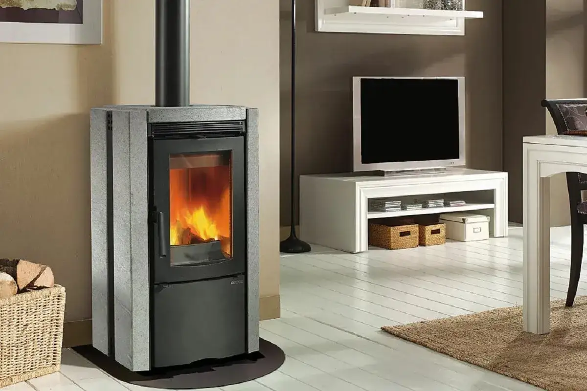 Estufa de leña moderna, uno de los tipos de estufas que calientan el hogar. Chimenea, leña y TV al fondo.