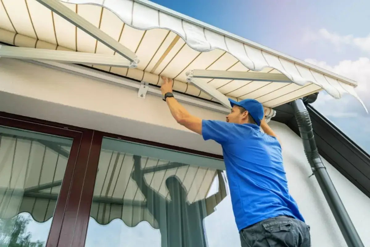 Un hombre con gorra azul ajusta la tela de un toldo, preparándose para cambiarla.