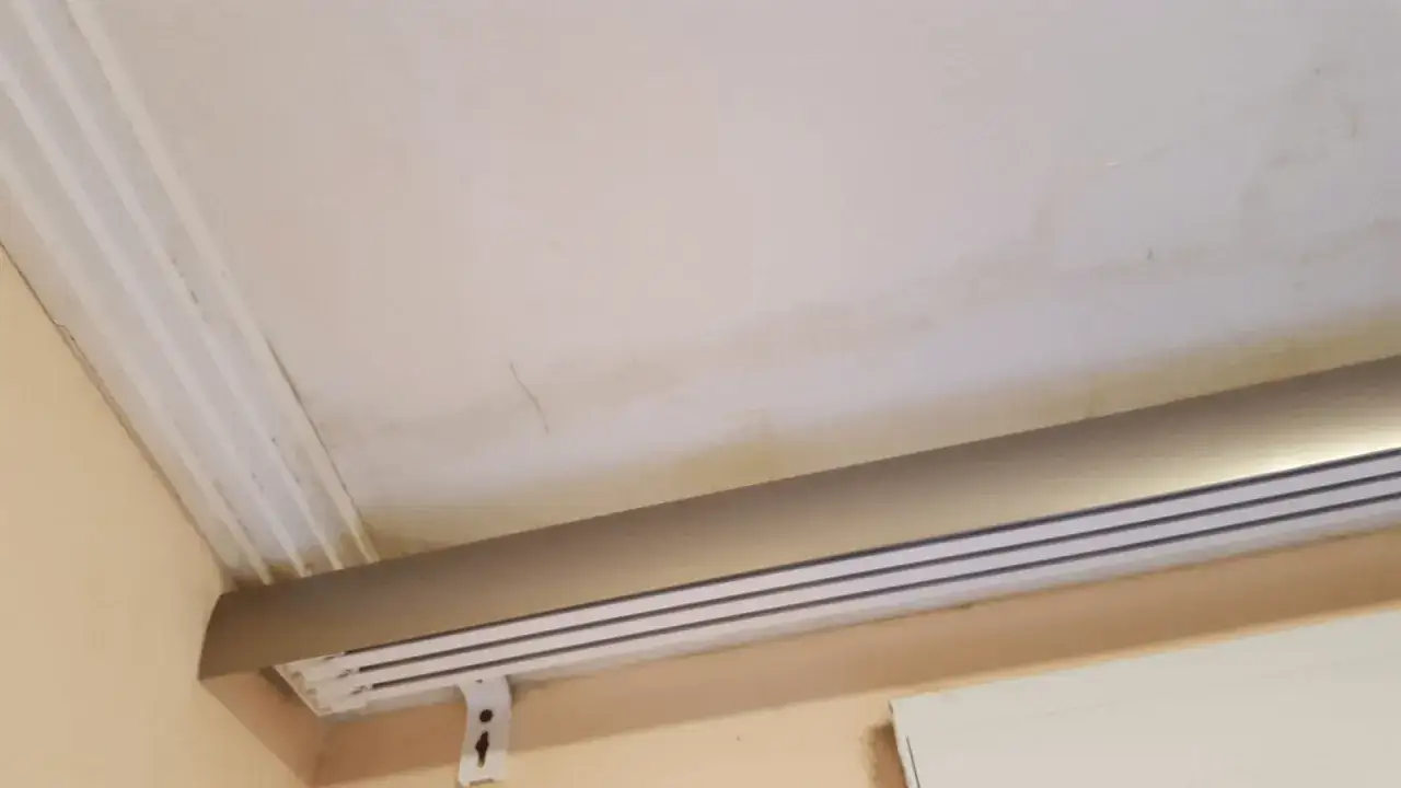 Manchas de moho en la pared y el techo, cerca de un riel de cortina.