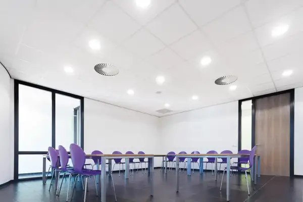 Sala de reuniones con sillas moradas y mesa. El falso techo blanco con luces empotradas y rejillas de ventilación crea un ambiente moderno.