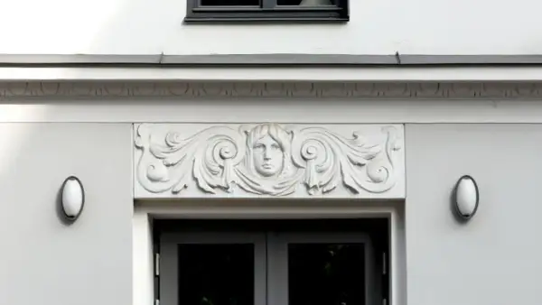 Detalle arquitectónico: una cornisa con un rostro femenino y volutas decorativas sobre una puerta.