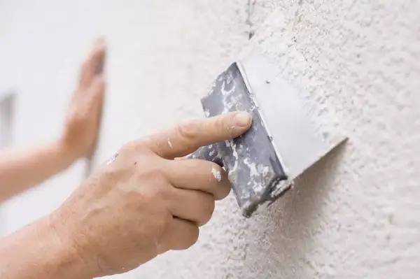 Mano aplicando masa para reparar gotele en una pared texturizada.