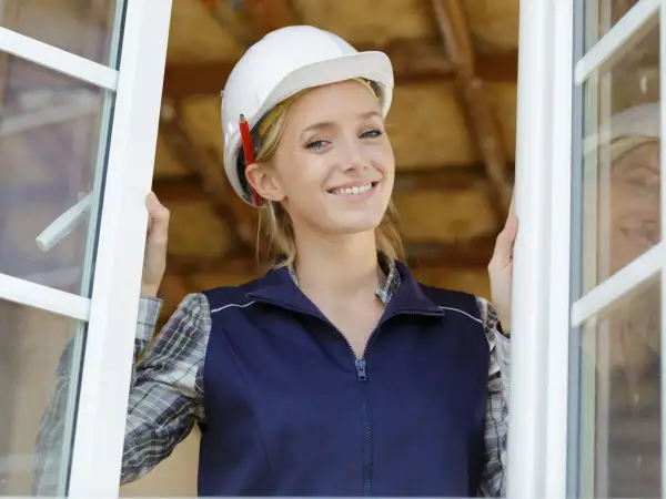 Mujer con casco y lápiz, sonriendo al abrir una ventana. Cumple la normativa de ventanas para viviendas.