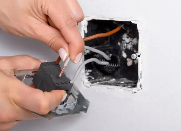 Manos conectando cables a un interruptor conmutador dentro de una caja empotrada en la pared.