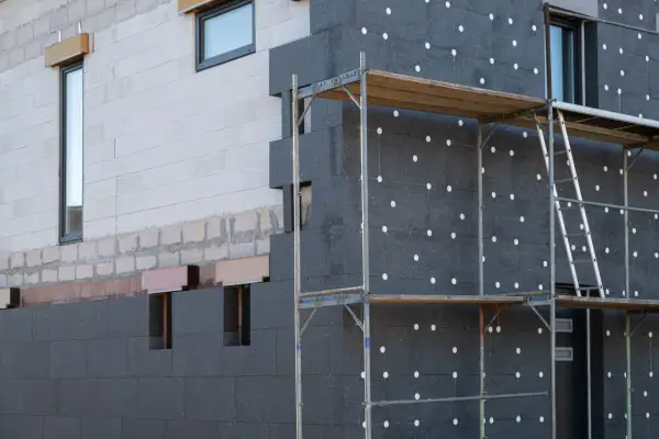 Fachada de edificio en construcción con aislamiento de poliestireno expandido gris, conocido como llana mineral, y andamios.