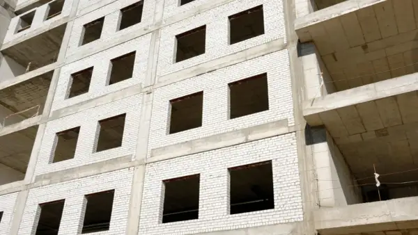 Fachada monocapa blanco de edificio en construcción, con ventanas vacías y balcones de hormigón.