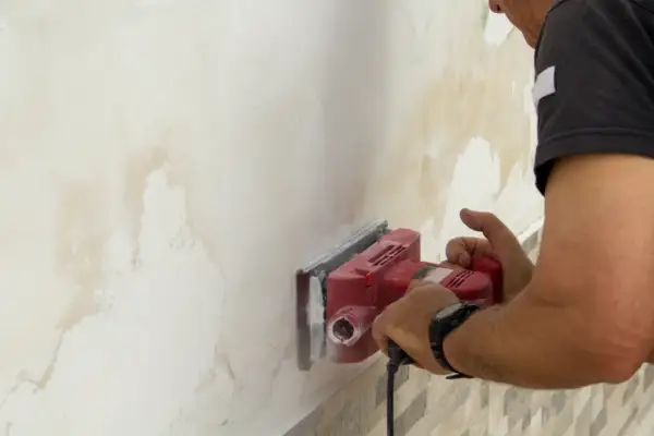 Hombre lijando pared con manchas de humedad para arreglar humedades.