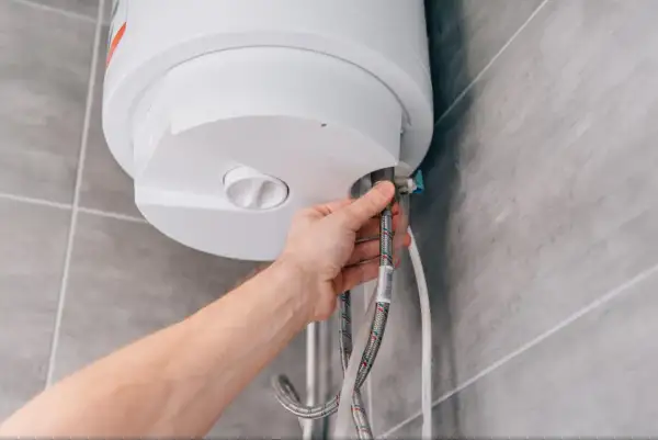 Mano conectando mangueras a un termo eléctrico. Guía para saber como vaciar un termo eléctrico de forma segura.