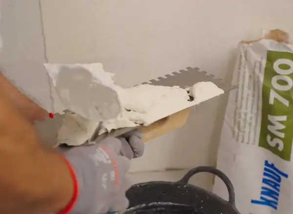 Man applying morteros para fachadas con llana dentada. Bolsa de producto de construcción al fondo.