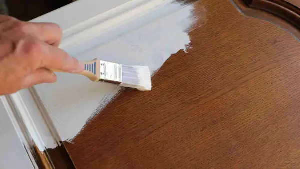 Mano pintando una puerta de madera con brocha blanca. El proceso de pintar puertas de madera es un proyecto de bricolaje común.